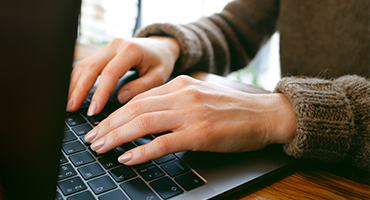 Hands and arms of a person wearing a sweater and typing on a laptop to illustrate employee health care solutions blog post. 