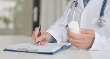 A doctor filling out paperwork while holding a prescription bottle to illustrate prescription benefits management services. 