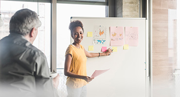 Two coworkers, a woman and a man, working out a self-funded benefits plan business problem on a white board.