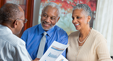 A black man with glasses holding a paper talks to a smiling black couple to show client success demonstrated in HealthNow case studies.  