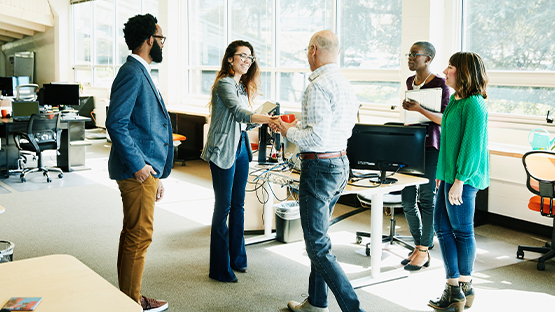 A man shakes a woman’s hand as three others look on in a workplace to illustrate the strength of HealthNow partnerships.